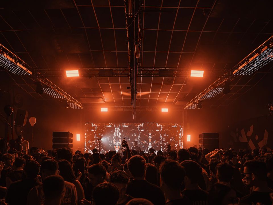 Packed club with orange lights and an LED wall with visuals behind the DJ