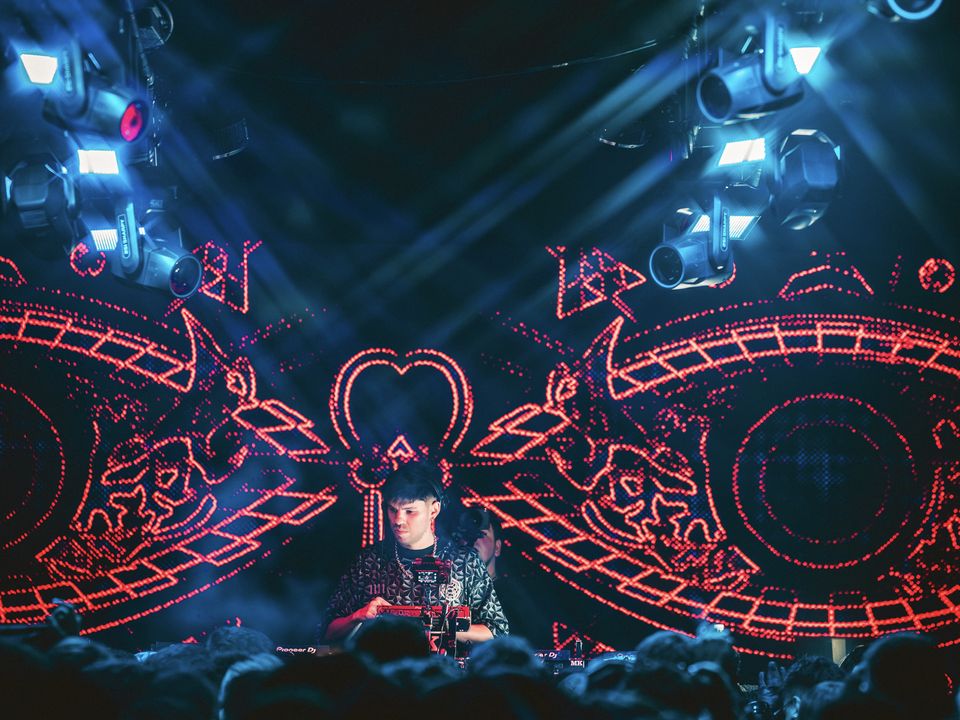 DJ in front of an LED wall with red visuals and blue moving heads above